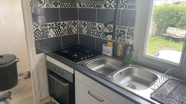 Et køkken med gaskomfur, ovn, dobbeltvask og et mønstret backsplash.