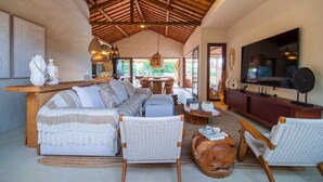 A spacious living area with a high ceiling, a large TV, and a comfortable seating arrangement including a sofa and chairs. - Casa com Piscina e Quadra no Condom nio By Toque (São Miguel dos Milagres)
