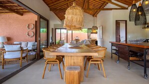 A spacious dining area with a large wooden table surrounded by wicker chairs, a hanging light fixture, and a rustic ceiling. - Casa com Piscina e Quadra no Condom nio By Toque (São Miguel dos Milagres)