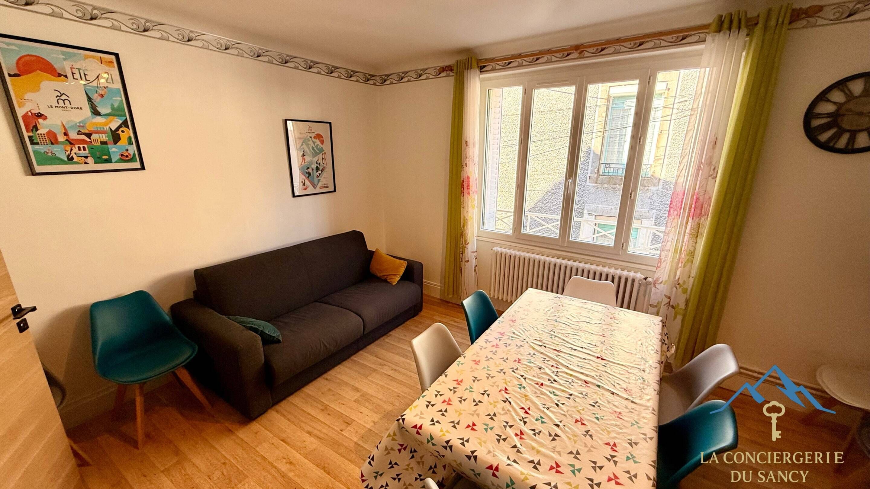 Ein gemütliches Wohnzimmer mit einer Couch, Sesseln, einem Esstisch und einem fenster mit Vorhängen.