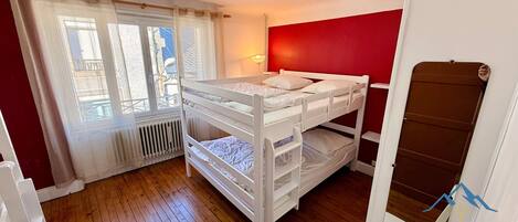 A bunk bed room with a red wall, a window with curtains, and a radiator.