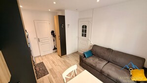A living room with a brown sofa, a white table, and a door leading to another room. - Alpine Sanctuary by the Market Lane (Mont-Dore)
