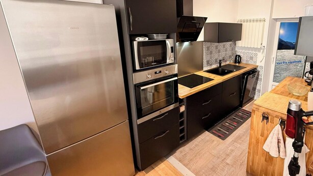 A modern kitchen with a stainless steel refrigerator, double ovens, a microwave, and a wooden countertop. - Alpine Sanctuary by the Market Lane (Mont-Dore)