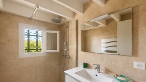 Un baño con ducha, lavamanos, espejo y una ventana con celosía decorativa.