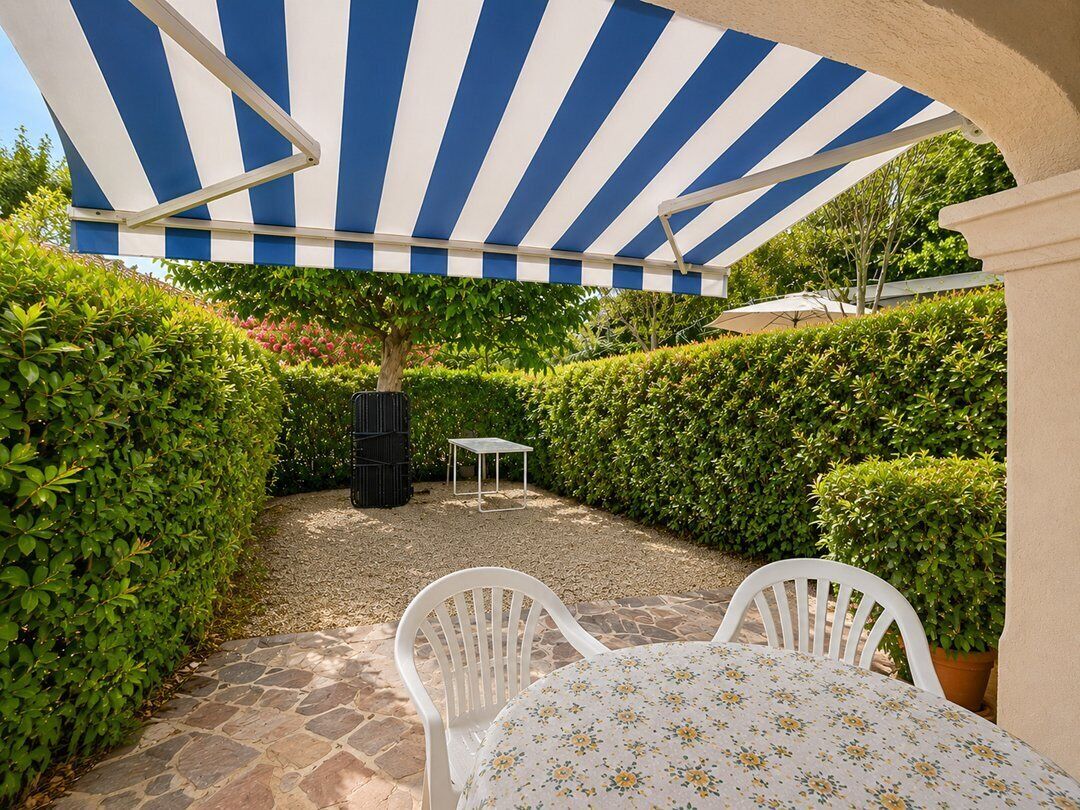 An outdoor patio area with a striped awning, a table with chairs, and a small table in the background.
