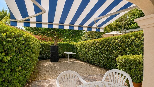 Un patio al aire libre con toldo a rayas, una mesa con sillas y una mesa pequeña al fondo.