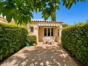 A patio with a table and chairs, surrounded by hedges and a building with a tiled roof. - Charming and Quiet Cottage – Sainte-Maxime (STE MAXIME)