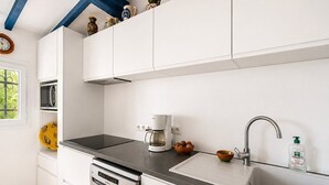 Una cocina moderna con armarios blancos, encimera negra, cafetera, fregadero y botella de lavavajillas.