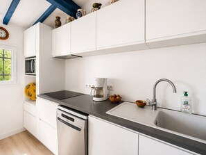 A modern kitchen with white cabinets, a black countertop, a coffee maker, a sink, and a dish soap bottle. - Charming and Quiet Cottage – Sainte-Maxime (STE MAXIME)