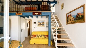 Una habitación con escalera de madera, un sofá amarillo, una cama con ropa de cama floral y un cuadro en la pared.
