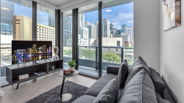 A modern living room with a large TV, a sofa, and a balcony with a city view. - Downtown Miami Worldcenter Studio, Pool & Balcony (Miami)
