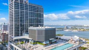 A high-rise hotel with a rooftop pool, a view of the city skyline, and a body of water in the background. - Downtown Miami Worldcenter Studio, Pool & Balcony (Miami)