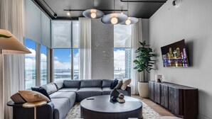 A modern living room with a sectional sofa, a round coffee table, and a large window offering a city view. - Downtown Miami Worldcenter Studio, Pool & Balcony (Miami)