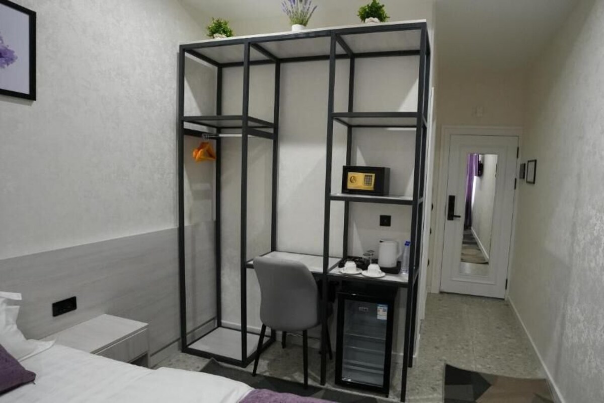 A compact room with a bed, a desk with a chair, a small kitchenette, and a glass partition.