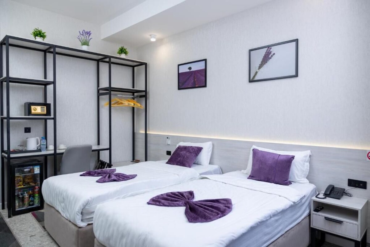 A hotel room with two beds, a desk with a computer, a mini-fridge, and a small seating area.