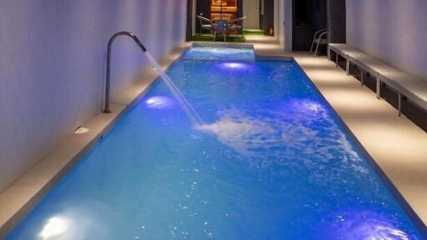 En moderne indendørs swimmingpool med et stjernedrysset loft og udsigt til et rum med pejs.