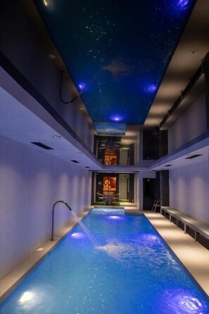 Una piscina interna moderna con un soffitto a stelle e vista su una stanza con un camino.