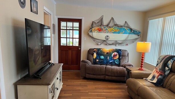 A living room with a television, a couch, a recliner, and a surfboard decoration.