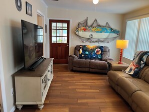 Una sala de estar con televisión, un sofá, un sillón reclinable y una decoración con una tabla de surf.