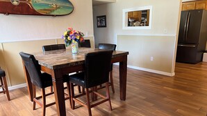 A dining area with a wooden table and chairs, a vase with flowers, and a kitchen in the background.