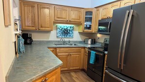 A kitchen with wooden cabinets, a stainless steel refrigerator, a microwave, and a sink.