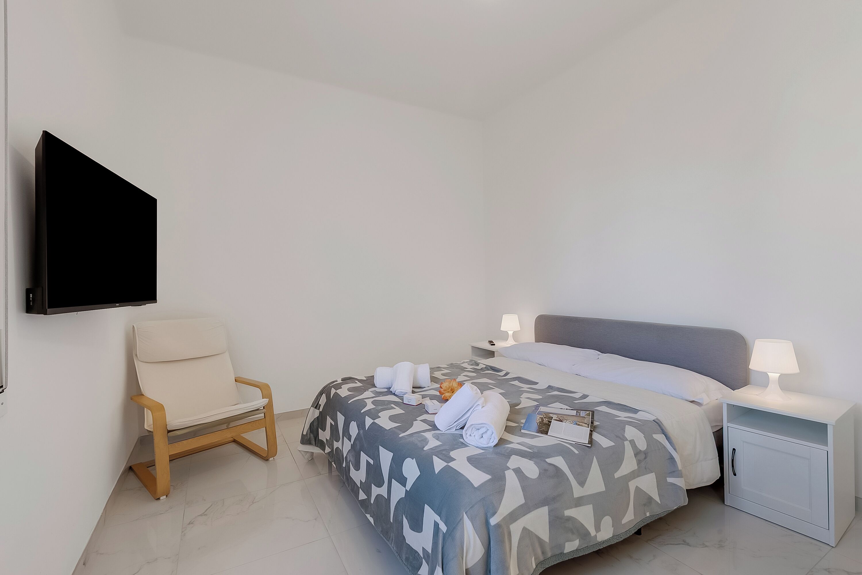 A hotel room with a bed, a chair, a nightstand, a TV, and a lamp.
