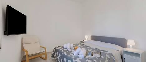 A hotel room with a bed, a chair, a nightstand, a TV, and a lamp.