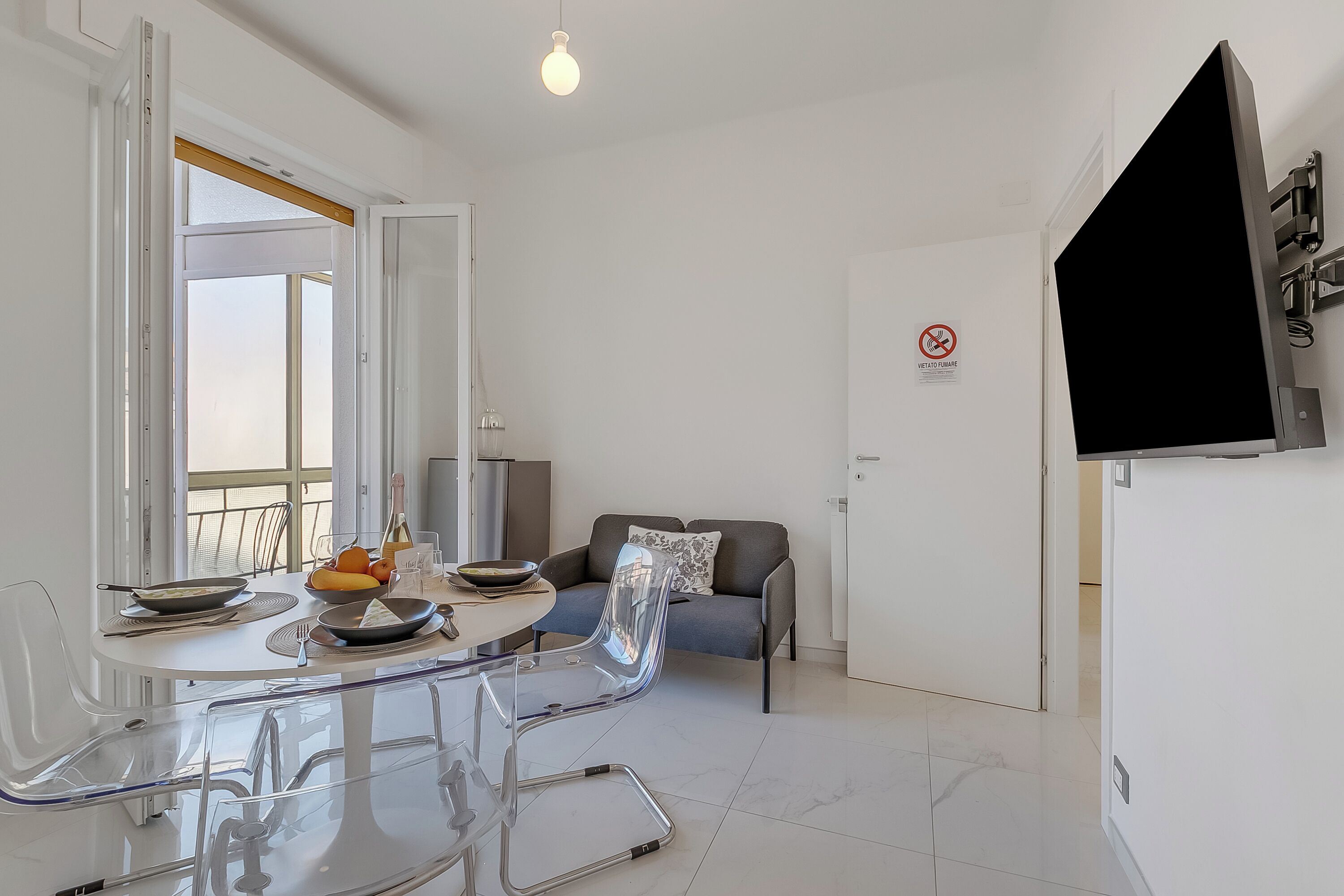 A modern living room with a dining table, chairs, a sofa, and a TV mounted on the wall.