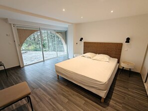 Ein Schlafzimmer mit einem großen Bett, einer Bank, einem kleinen Tisch und einer Schiebeglastür zu einem Außenbereich.