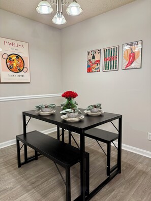 A dining area with a black metal table and bench, a vase of red roses, and three plates with a green bottle. - Quiet & Cozy Nook, Prime Location Near Everything! (Atlanta)