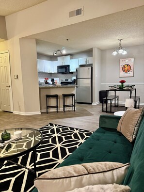 A modern living room with a green sofa, a glass coffee table, and a patterned rug. - Quiet & Cozy Nook, Prime Location Near Everything! (Atlanta)