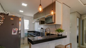 Een moderne keuken met een centraal eiland, roestvrijstalen apparatuur, hanglampen en een potplant.
