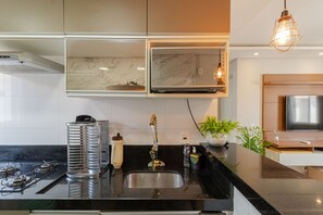 Une cuisine moderne avec un plan de travail noir, des appareils en acier inoxydable, un four encastré et un luminaire suspendu.
