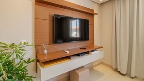 Een moderne woonkamer met een grote flatscreen televisie bevestigd aan een houten wandmeubel, een kleine tafel met een afstandsbediening en een potplant.