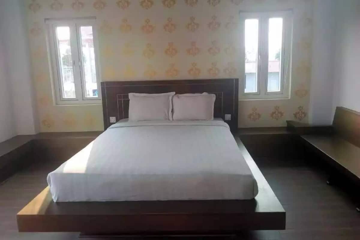 A bedroom with a bed, two windows, and a patterned wall.