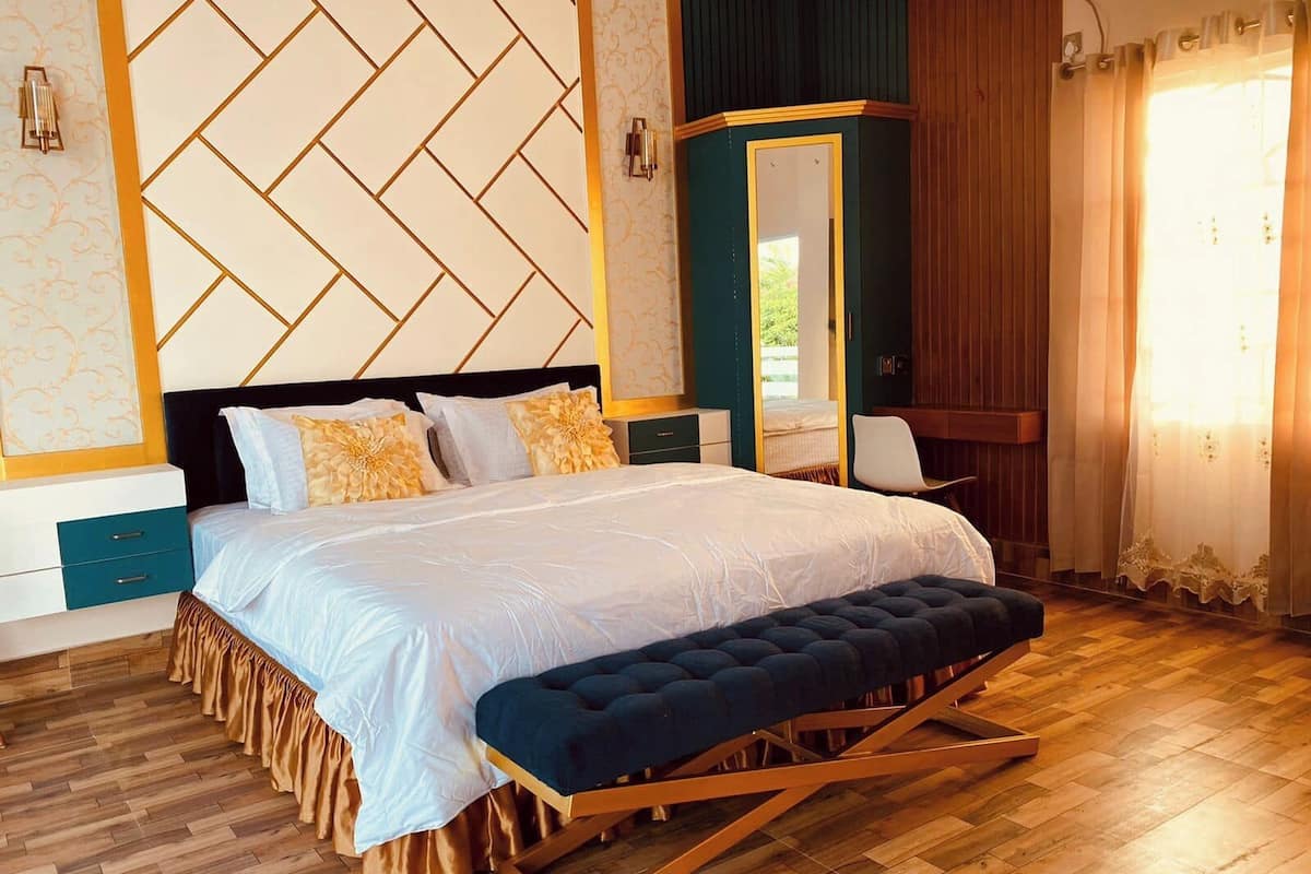 A bedroom with a large bed, a bench, a dresser, and a mirror.