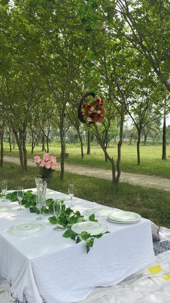An outdoor dining setup with a table set for six, surrounded by greenery and trees.