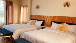 Een hotelkamer met twee bedden, een bankje, houten vloeren en een raam met gordijnen.