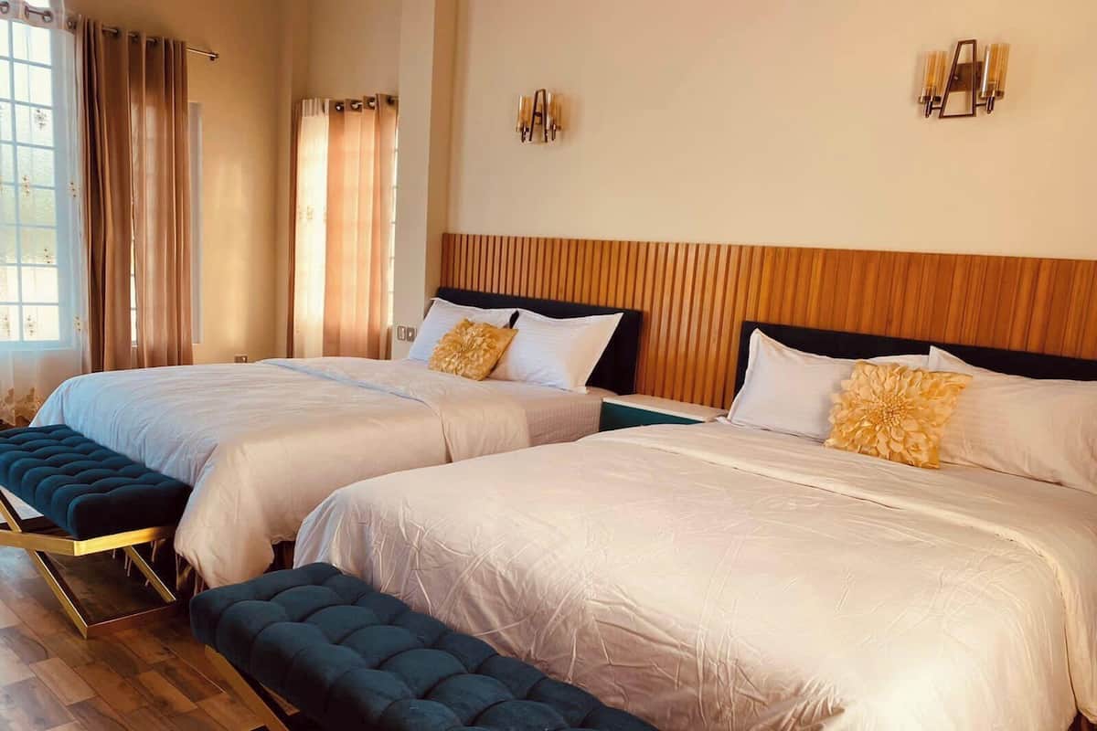 A hotel room with two beds, a bench, wooden flooring, and a window with curtains.