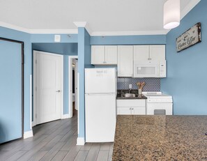 A kitchen with blue walls, white cabinets, a granite countertop, and a refrigerator. - Cozy oceanfront 1-bedroom condo in beautiful Myrtle Beach (Myrtle Beach)