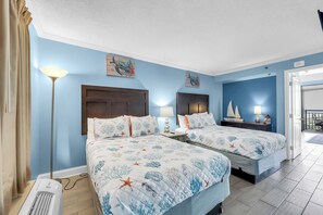A hotel room with two beds, a ceiling fan, a nightstand with a lamp, and a view of the outside balcony. - Cozy oceanfront 1-bedroom condo in beautiful Myrtle Beach (Myrtle Beach)