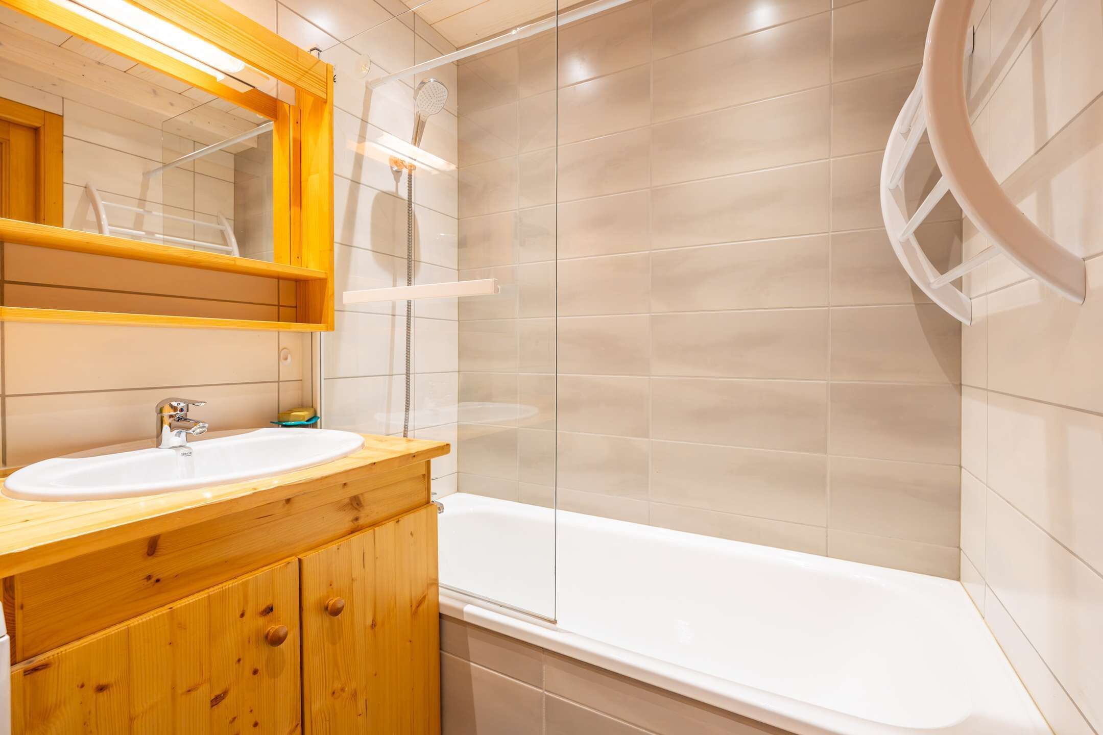 A modern bathroom with a wooden vanity, a white sink, and a bathtub.