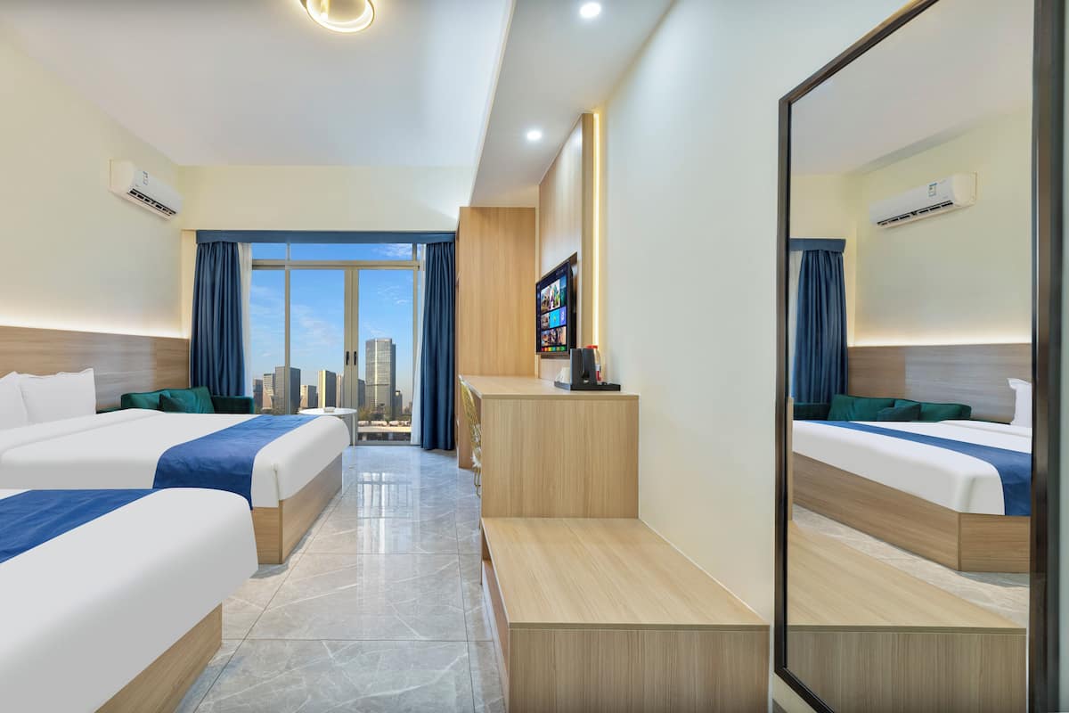 A hotel room with two beds, a TV, a desk, and a city view.
