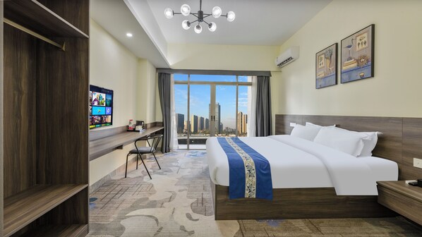 Een hotelkamer met een groot bed, een bureau met stoel, een televisie en uitzicht op de stad.