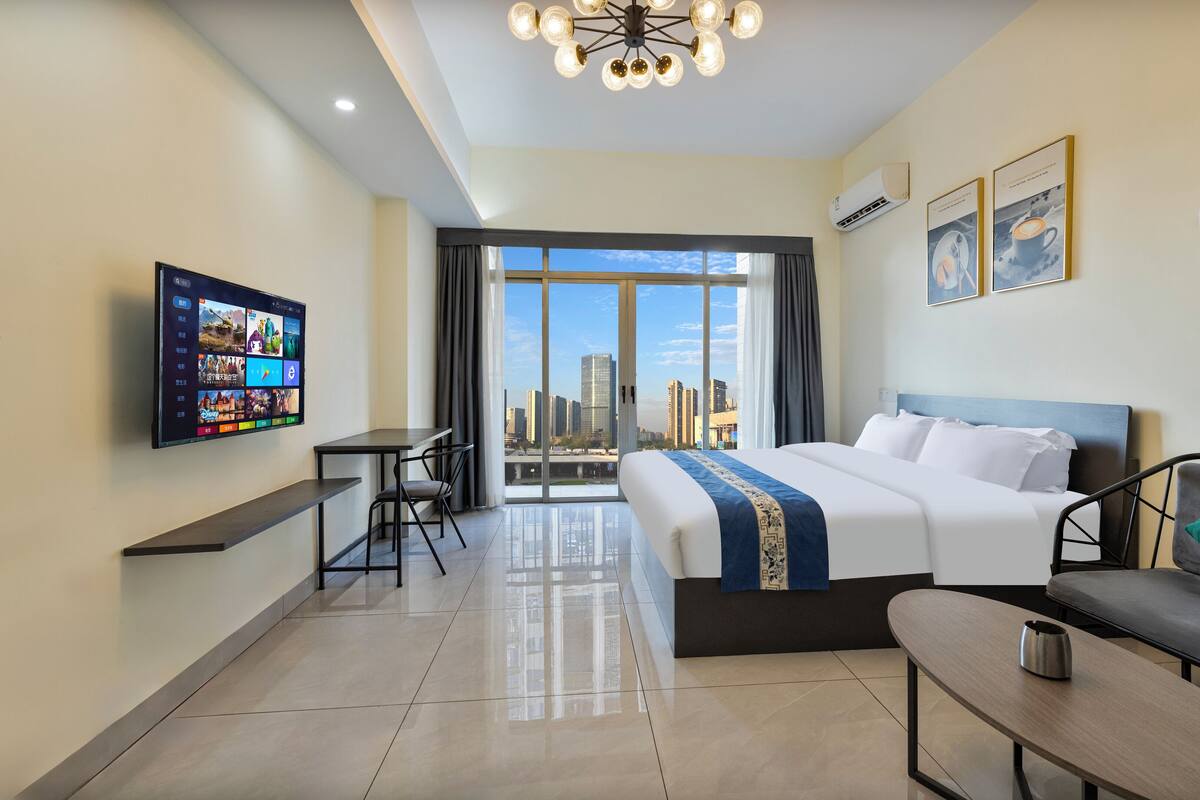 A hotel room with a bed, a desk, a chair, a TV, and a view of the cityscape.
