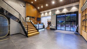 Een moderne lobby met een trap, receptiebalie en glazen deuren naar buiten.