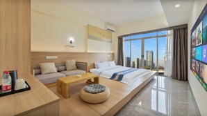 Een moderne hotelkamer met een bed, bank, salontafel en een groot raam met uitzicht op de stad.