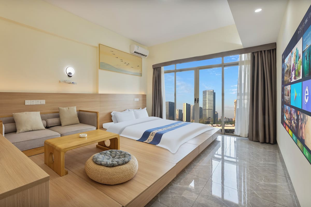 A modern hotel room with a bed, sofa, coffee table, and a large window with a city view.