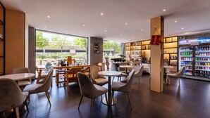 Een modern café met tafels, stoelen, een boekenkast en een drankkoelkast.