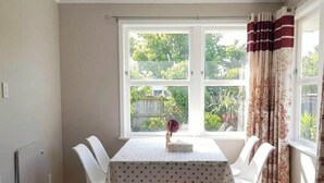 Un comedor con una mesa dispuesta para cuatro personas, una ventana con cortinas y vista a zonas verdes.